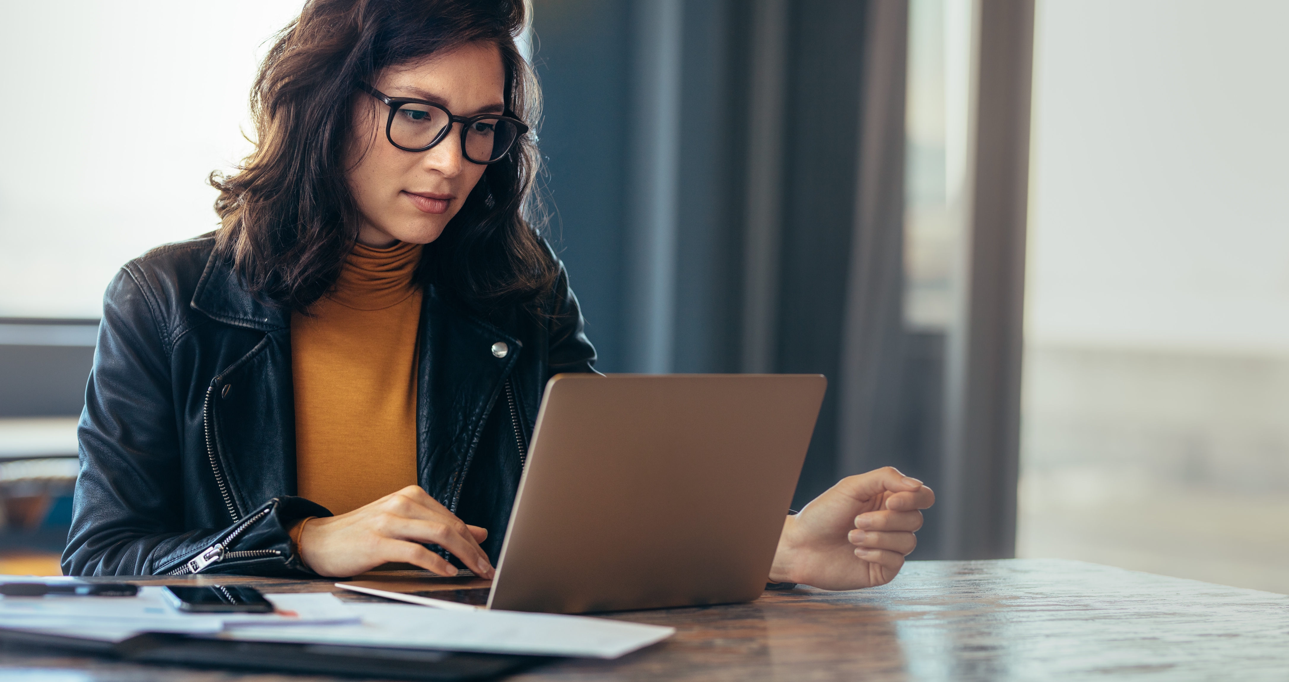 A woman wearing glassed working at a laptop whilst sat at a desk